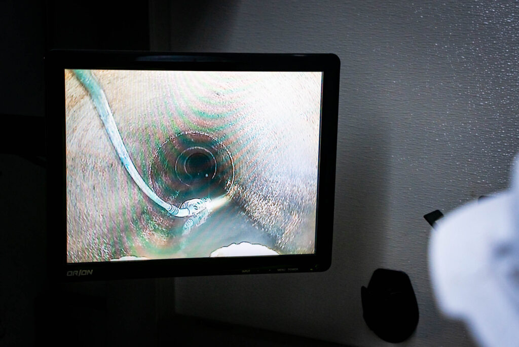 A technician operates a CCTV camera for pipe inspection, focusing on the monitor displaying the interior of a pipeline.