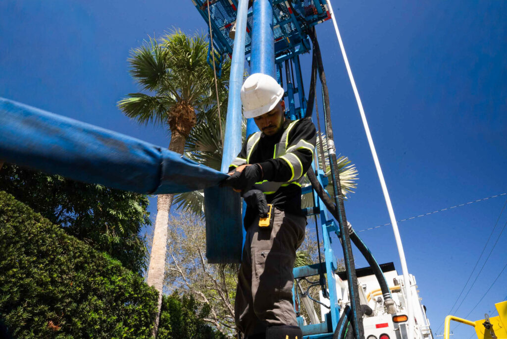 A worker in a hard hat and safety vest inspects a large, flexible pipe liner in an industrial setting, showcasing CIPP lining