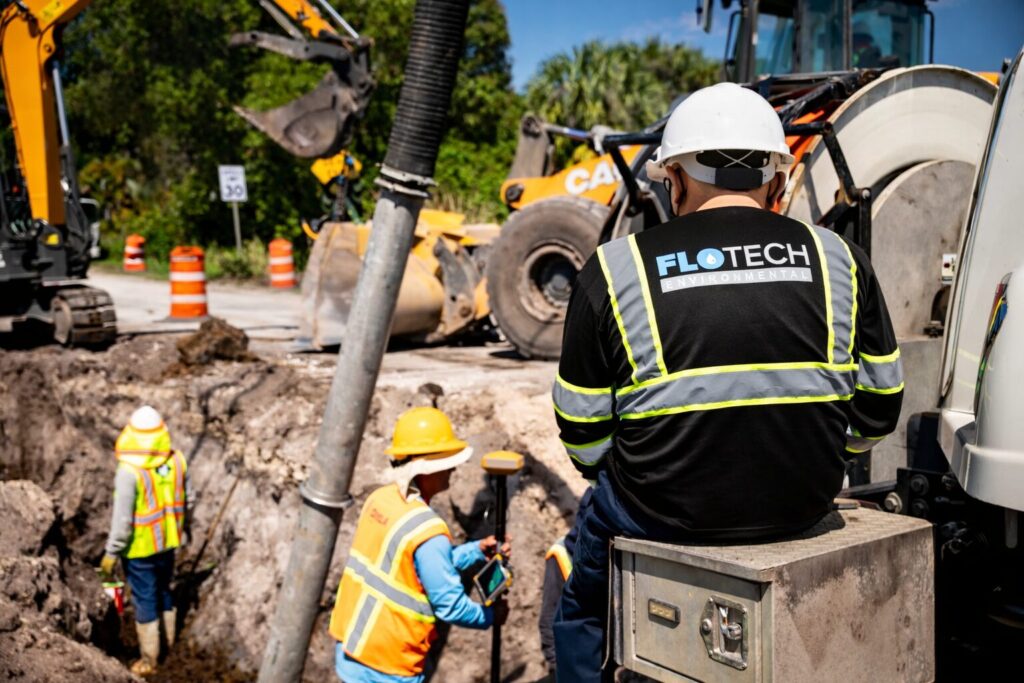 A hydro excavation truck with a large hose is parked on a construction site, surrounded by dirt and construction equipment.