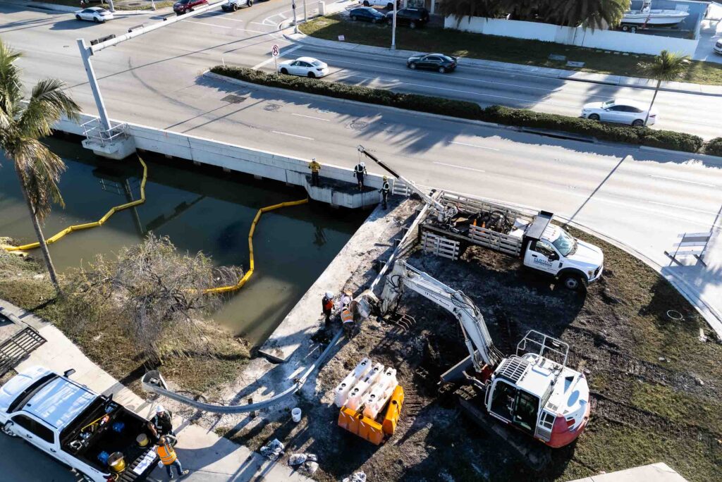 A jet vac truck performing cleaning operations on a city street, with hoses connected to a manhole, surrounded by safety cone